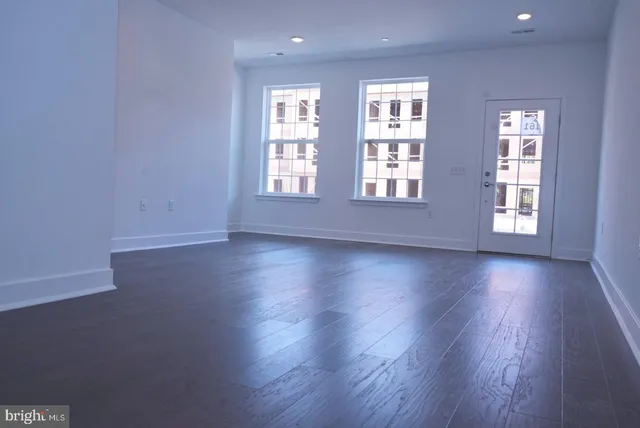 an empty room with wooden floor and windows with curtains