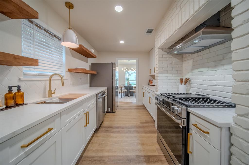 5125 Ashbrook Road Dallas, TX 75227 - Photo 16 of 34 Kitchen featuring white shaker cabinetry, gold-tone hardware, wood-finish flooring, stainless steel appliances, and a white brick-style backsplash
