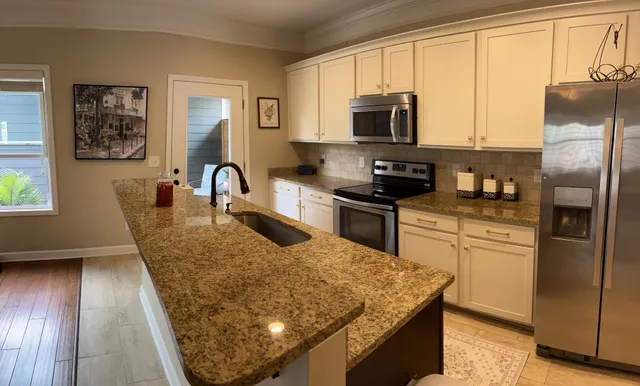 a kitchen with stainless steel appliances granite countertop a refrigerator a stove top oven a sink a dining table and chairs with wooden floor