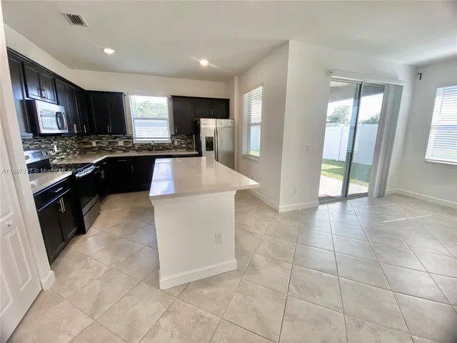 a large kitchen with kitchen island granite countertop a stove a sink a counter space and cabinets