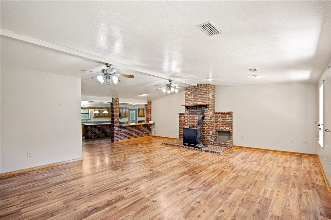 655 Charton Road Morrilton, AR 72110 - Photo 5 of 49 Spacious living area featuring wood-finish flooring, a prominent brick fireplace with a wood-burning stove, and multiple ceiling fans