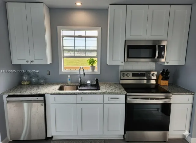 a kitchen with granite countertop white cabinets sink and stainless steel appliances