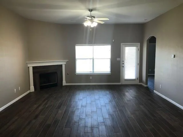 a view of an empty room with wooden floor fireplace and a window