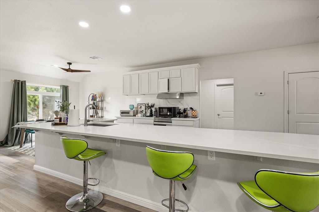 4801 West Wedgefield Road Granbury, TX 76049 - Photo 4 of 40 a kitchen with stainless steel appliances granite countertop a sink a stove a dining table and chairs with wooden floor