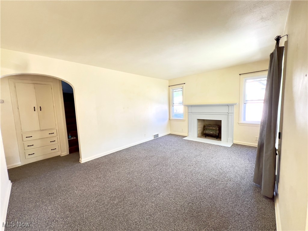 Unfurnished living room featuring a healthy amount of sunlight and dark carpet