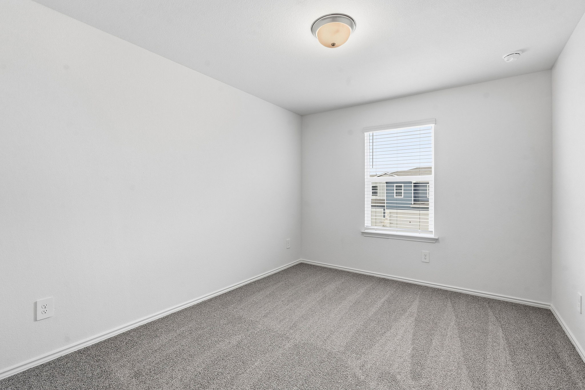 164 Cinnabar Lane, Unit 5 Kyle, TX 78640 - Photo 16 of 21 Light-filled room featuring neutral wall paint, gray carpet flooring, a single window with blinds, and a ceiling-mounted light fixture