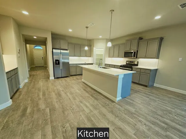 a large kitchen with stainless steel appliances granite countertop a stove a sink dishwasher a refrigerator and white cabinets with wooden floor