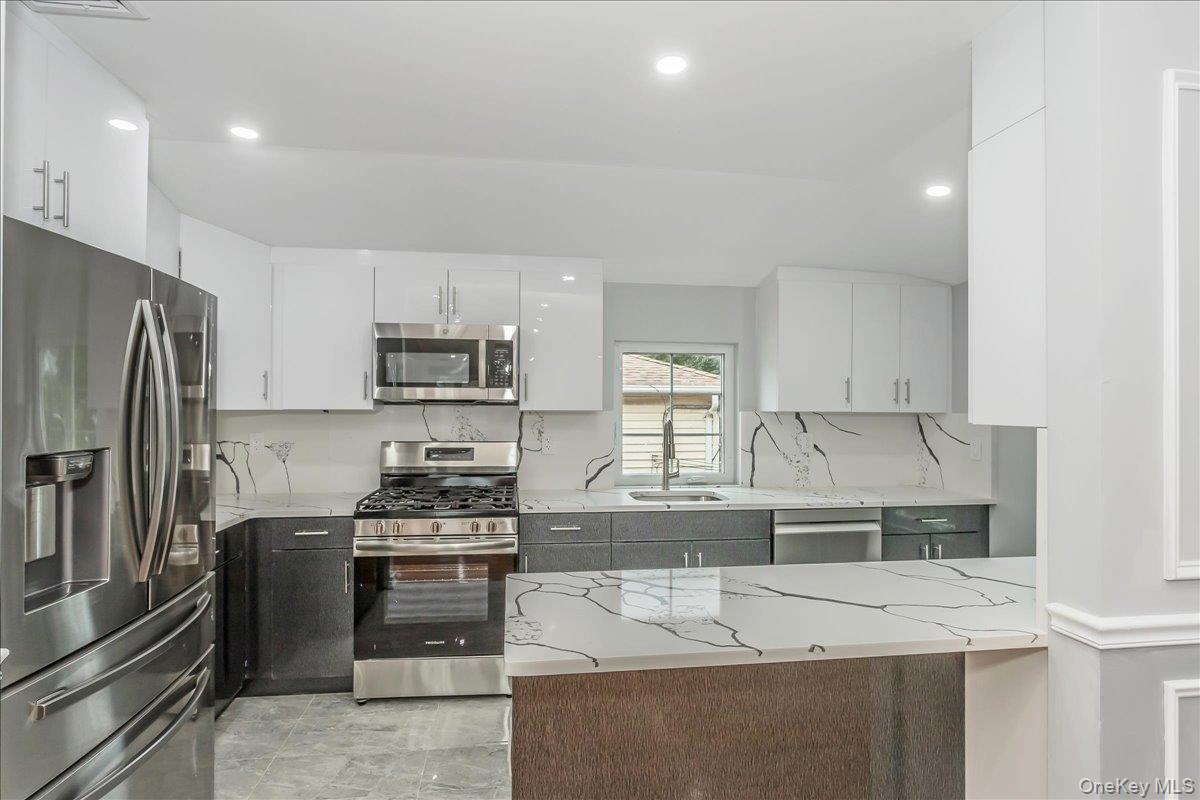 243-36 Caney Road Queens, NY 11422 - Photo 18 of 30 Kitchen with appliances with stainless steel finishes, white cabinetry, light stone counters, and recessed lighting