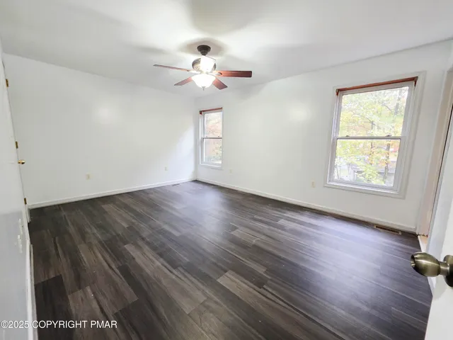an empty room with wooden floor chandelier fan and windows