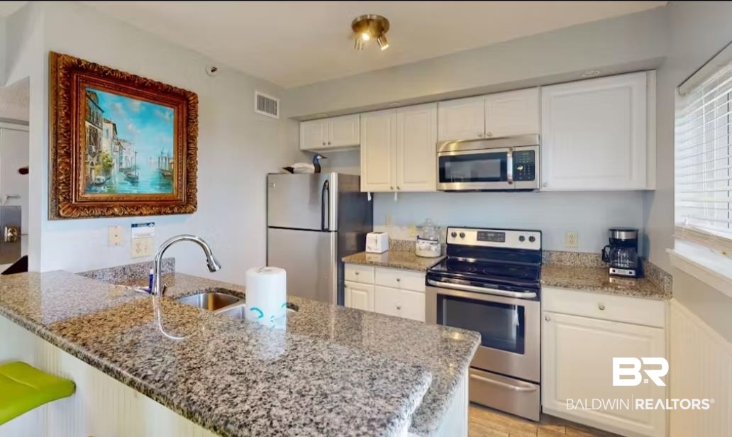 375 Plantation Road, Unit 5814 Gulf Shores, AL 36542 - Photo 10 of 31 Kitchen with kitchen peninsula, white cabinets, light stone countertops, sink, and stainless steel appliances