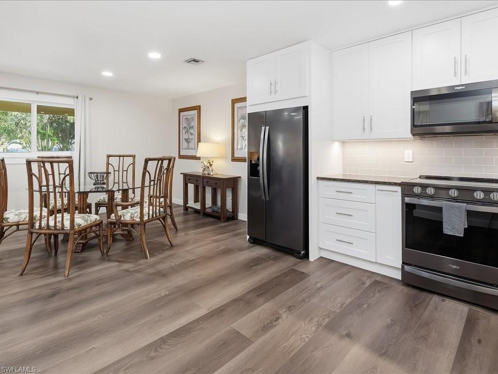 186 Harrison Road, Unit H2 Naples, FL 34112 - Photo 18 of 38 a kitchen with stainless steel appliances granite countertop a stove a refrigerator a microwave a dining table and chairs with wooden floor
