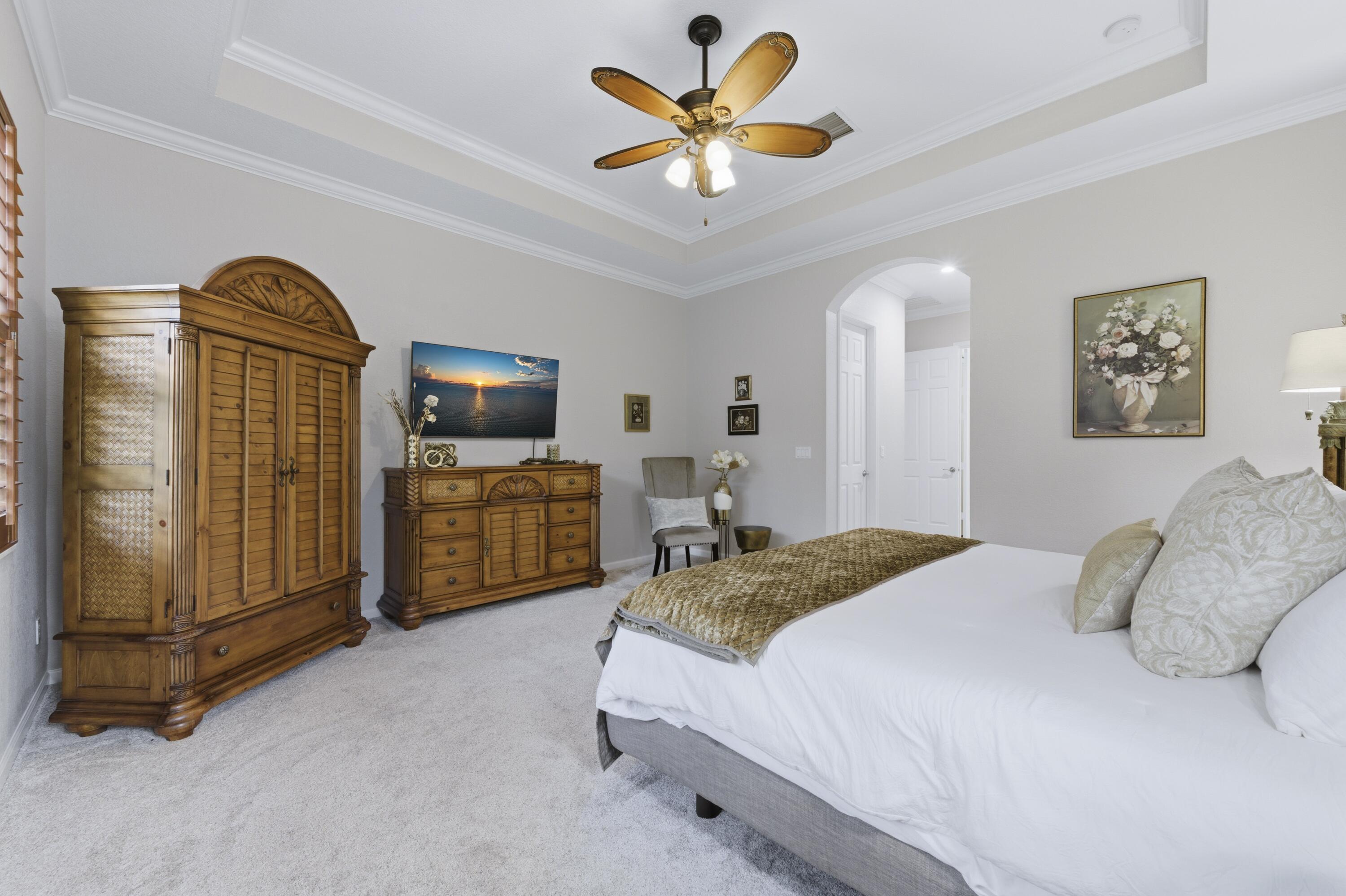 1016 Southwest Triste Way Stuart, FL 34997 - Photo 15 of 41 a spacious bedroom with a bed a flat screen tv and a chandelier
