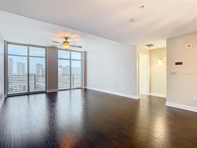 an empty room with wooden floor chandelier fan and windows