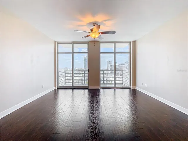 an empty room with wooden floor fan and windows