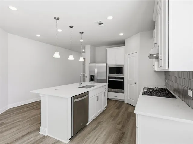a large kitchen with stainless steel appliances kitchen island granite countertop a stove a sink a refrigerator and white cabinets with wooden floor