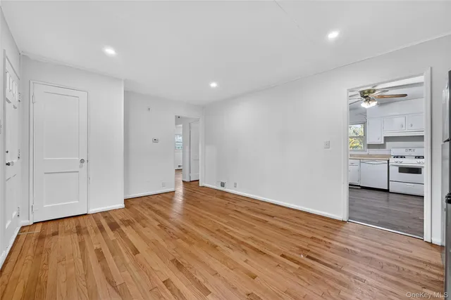 a view of an empty room with wooden floor and a kitchen