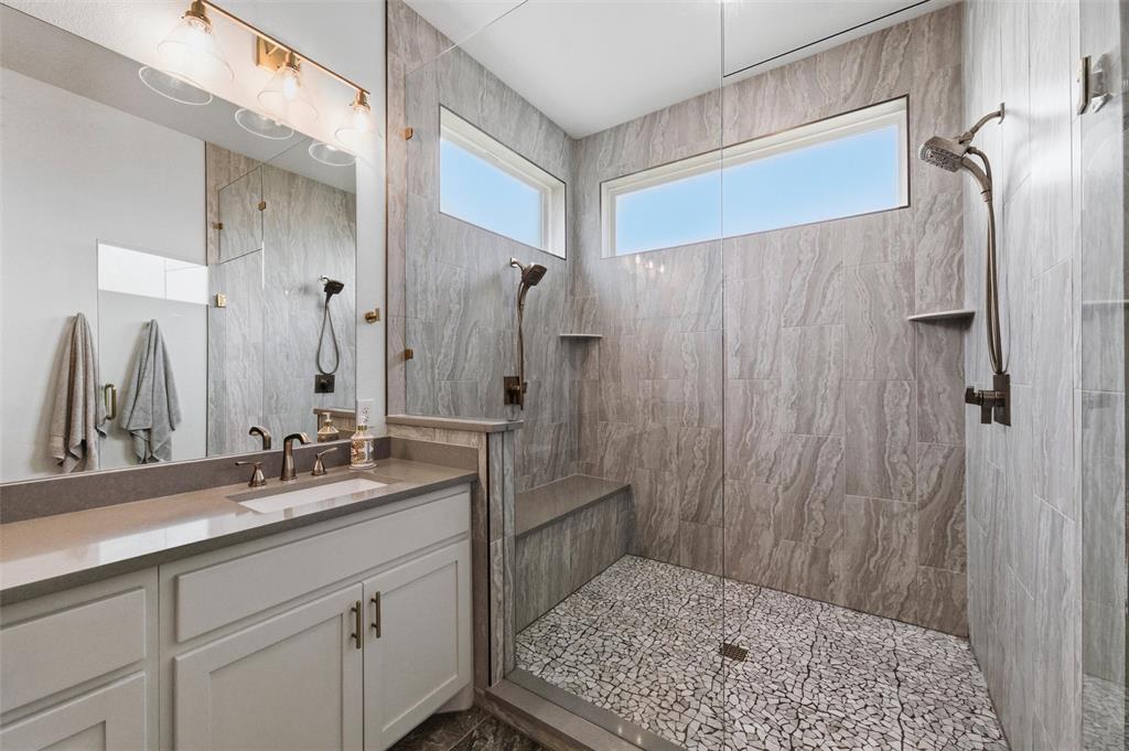 6625 Sandy Beach Road Azle, TX 76020 - Photo 17 of 40 Primary bathroom showcases oversized walk-in shower with full-height tile surround, pebble-style shower flooring, built-in bench seating, and dual vanity layout with extensive storage and modern fixtures throughout.