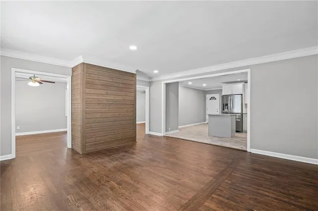 a view of empty room with wooden floor and kitchen