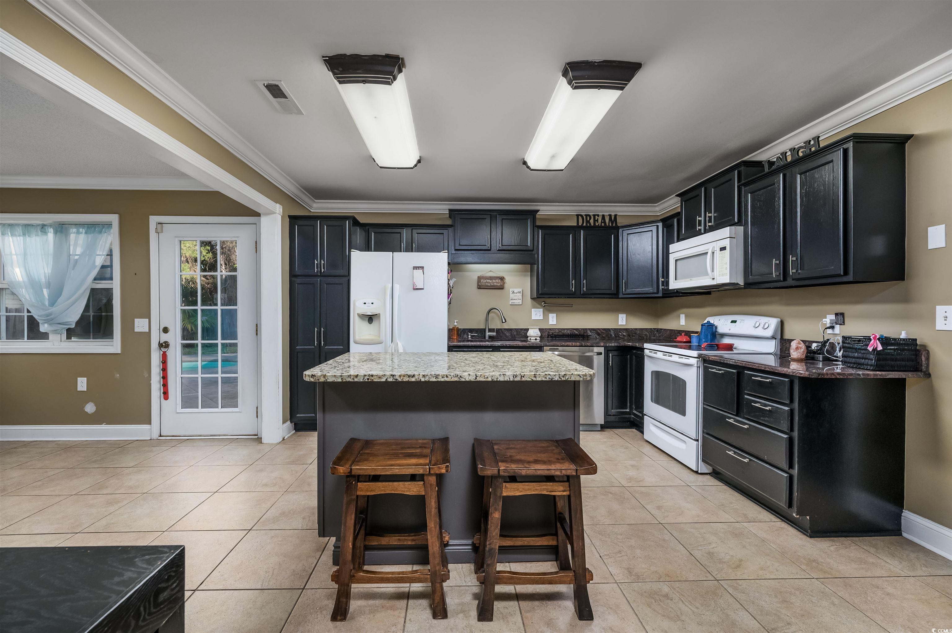 6252 Salem Road Myrtle Beach, SC 29588 - Photo 29 of 39 Kitchen with light stone countertops, light tile patterned flooring, white appliances, a kitchen island, and ornamental molding