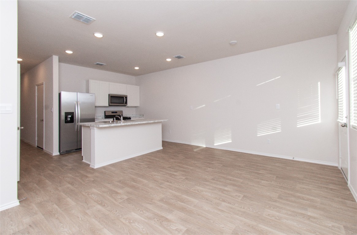 201 Varner Way Lockhart, TX 78644 - Photo 15 of 16 Kitchen featuring appliances with stainless steel finishes, an island with sink, white cabinets, open floor plan, and light wood-type flooring