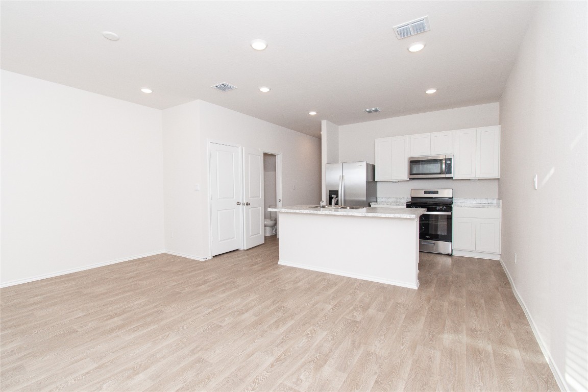201 Varner Way Lockhart, TX 78644 - Photo 16 of 16 Kitchen with appliances with stainless steel finishes, a center island with sink, open floor plan, white cabinetry, and light wood finished floors