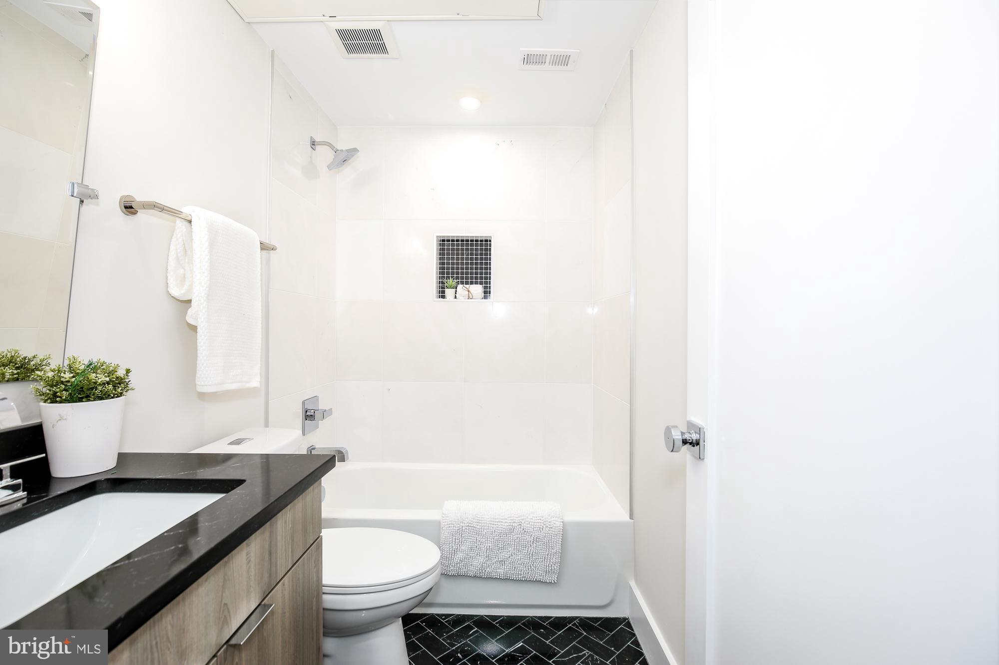 1421 Spring Road Northwest, Unit IZ204 Washington, DC 20010 - Photo 9 of 12 a bathroom with a granite countertop sink toilet a mirror and shower