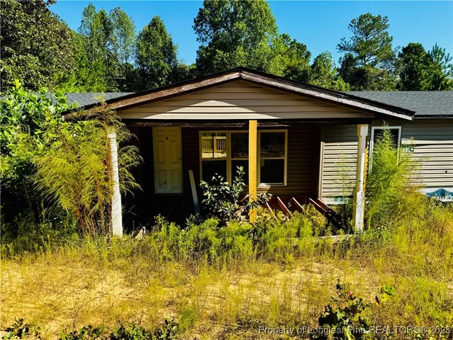 a view of a house with small yard plants and large tree