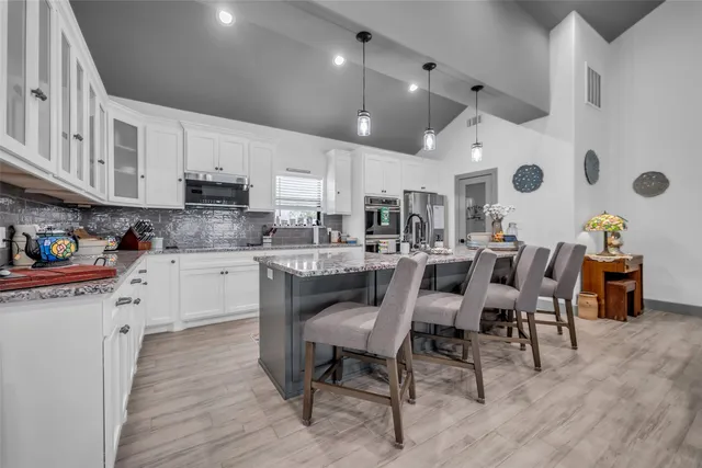 a kitchen with stainless steel appliances kitchen island granite countertop a table chairs sink and cabinets