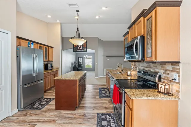 a kitchen with stainless steel appliances granite countertop a refrigerator a sink dishwasher a stove and a dining table with wooden floor