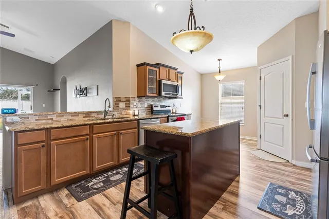 a kitchen with stainless steel appliances granite countertop a refrigerator a sink dishwasher a stove and a dining table with wooden floor