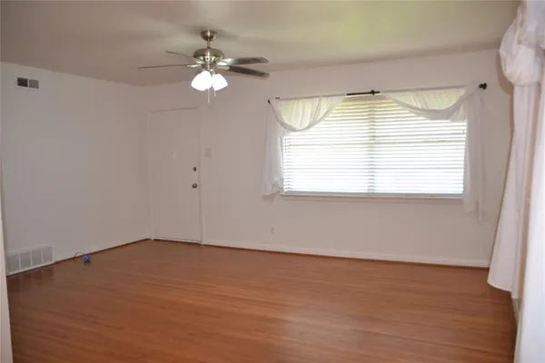 an empty room with wooden floor chandelier fan and windows