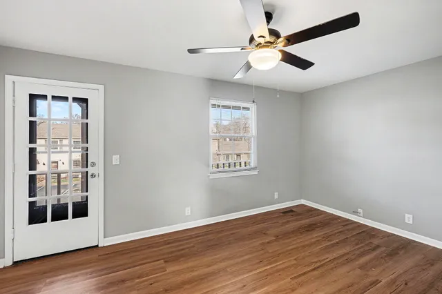 an empty room with wooden floor chandelier fan and windows
