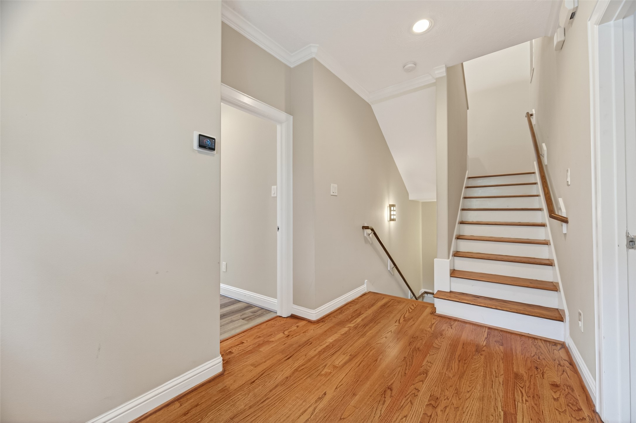 2611 Riverside Drive, Unit C Houston, TX 77004 - Photo 27 of 50 This bright and welcoming hallway features light-toned walls and beautiful hardwood flooring. A staircase with wood steps and a classic handrail leads to the upper level, while recessed lighting and a stylish wall-mounted fixture enhance the space. This area provides access to the spacious primary suite and a third bedroom with a private en suite, offering both functionality and a seamless flow throughout the home.