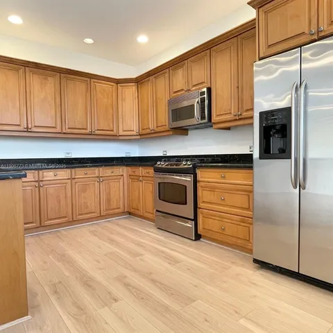 a kitchen with stainless steel appliances granite countertop a refrigerator a stove a sink and white cabinets with wooden floor