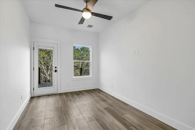 an empty room with wooden floor chandelier fan and windows