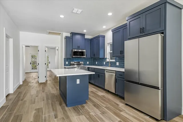 a kitchen with kitchen island granite countertop wooden floors stainless steel appliances a sink and a refrigerator