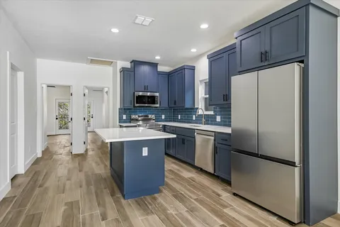 a kitchen with kitchen island granite countertop wooden floors stainless steel appliances a sink and a refrigerator