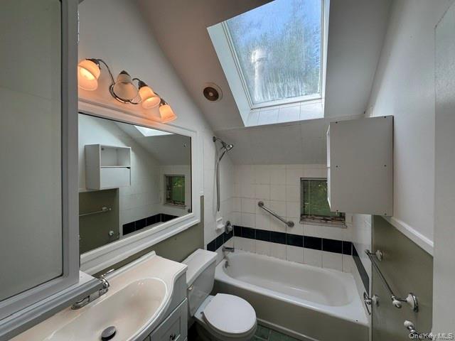 74 South Airmont Road Suffern, NY 10901 - Photo 23 of 42 Bathroom featuring a white bathtub, white tiled walls with a black accent stripe, and a skylight