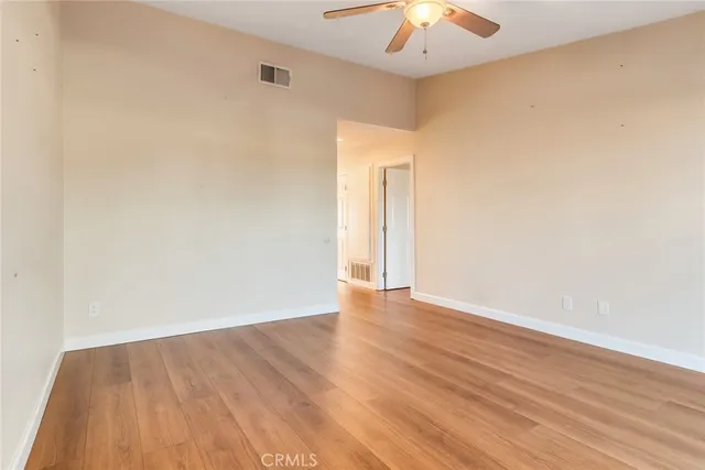 a view of an empty room with wooden floor and a ceiling fan