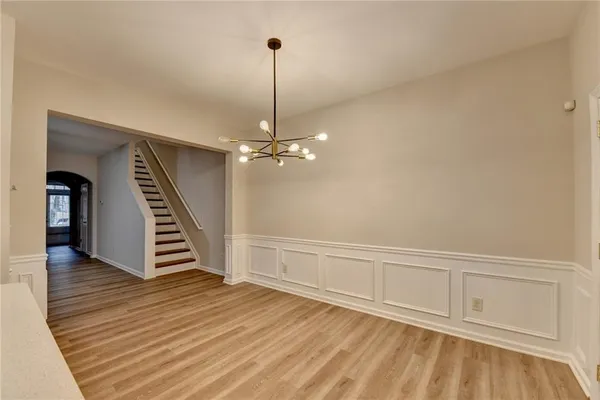 a view of an empty room with wooden floor stairs and a chandelier