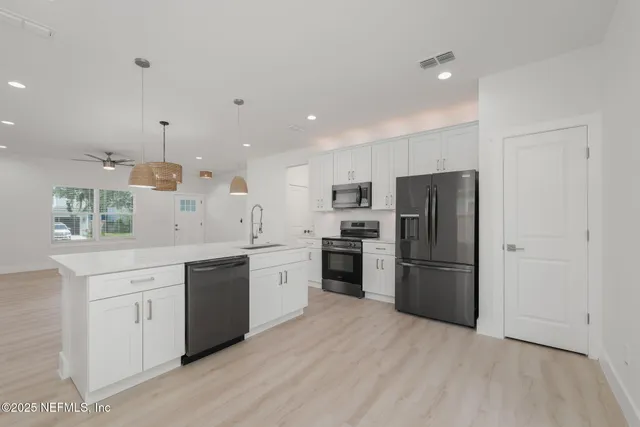 a large kitchen with a refrigerator a sink dishwasher a oven with white cabinets and wooden floor