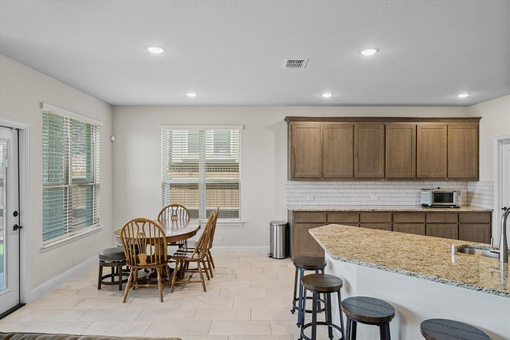 4102 Sublett Way Kaufman, TX 75142 - Photo 15 of 40 Kitchen featuring tasteful backsplash, a breakfast bar area, light stone counters, recessed lighting, and stainless steel microwave