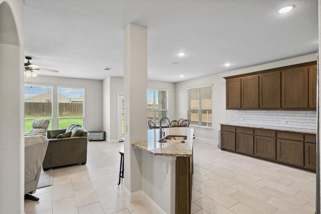 4102 Sublett Way Kaufman, TX 75142 - Photo 8 of 40 Kitchen featuring ceiling fan, backsplash, light stone countertops, light tile patterned floors, and plenty of natural light