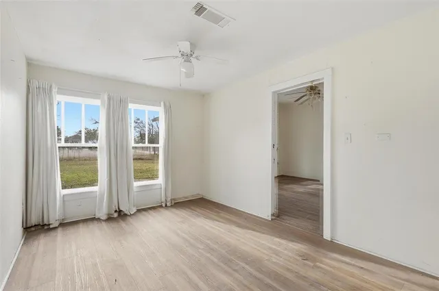 an empty room with wooden floor fan and windows