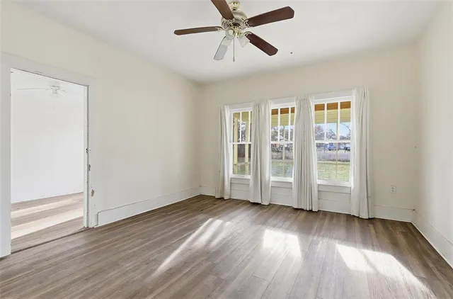 an empty room with wooden floor chandelier fan and windows