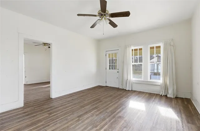 a view of an empty room with wooden floor and a ceiling fan