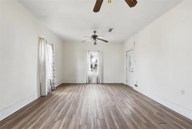 an empty room with wooden floor chandelier fan and windows