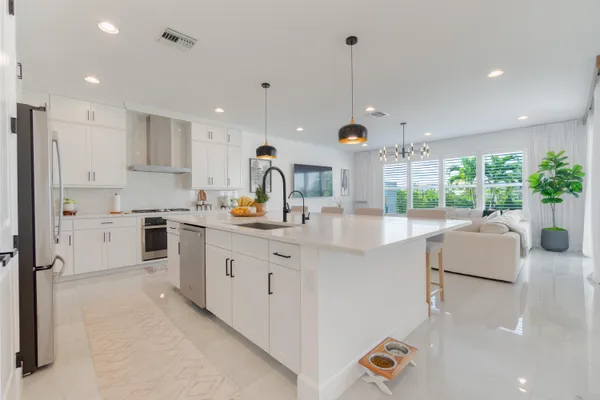 a kitchen with stainless steel appliances granite countertop a sink a stove a refrigerator and white cabinets with wooden floor