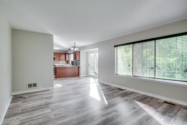 a view of empty room with wooden floor and kitchen view