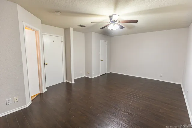 an empty room with wooden floor and fan